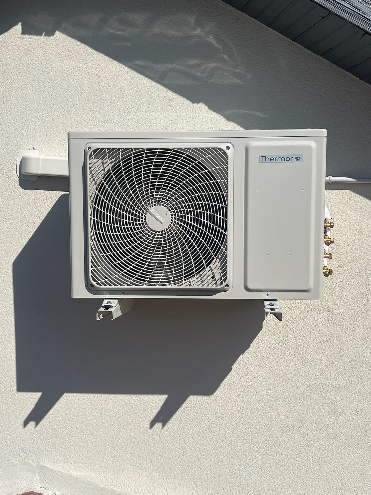Groupe extérieur de climatisation Thermor fixé en façade sous la toiture